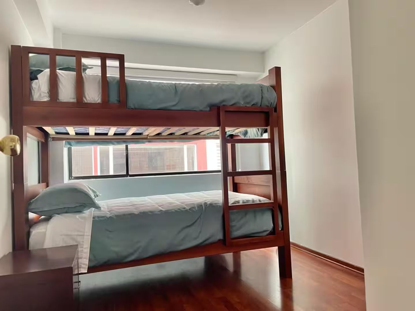 Ein Stockbett mit einer Leiter, ein Fenster mit Jalousien und ein Holzboden.