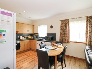 A compact kitchen with wooden cabinets, a microwave, and a dining area with a table and chairs. - The Old Store (Fort William)