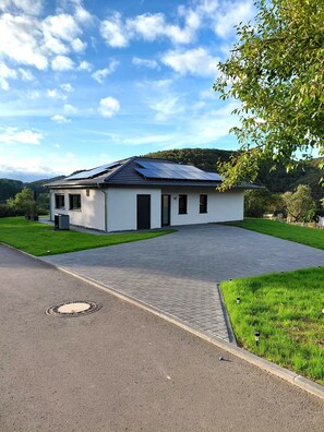 A modern single-story house with a paved driveway, solar panels on the roof, and a well-maintained lawn. - Ferienhaus Grünblick (Mauel)