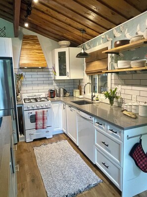 A modern kitchen with white cabinets, a stainless steel stove, and a wooden ceiling.
