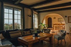 Ein gemütliches Wohnzimmer mit einem Holztisch, einer Couch und Blick durch große Fenster.