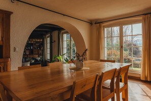 A dining area with a wooden table, chairs, and a view of the outdoors through large windows. - Large house with a private beach and its own dock (San Carlos de Bariloche)