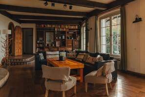 Een knus woongedeelte met een houten salontafel, twee fauteuils, een bank en een boekenkast vol boeken.