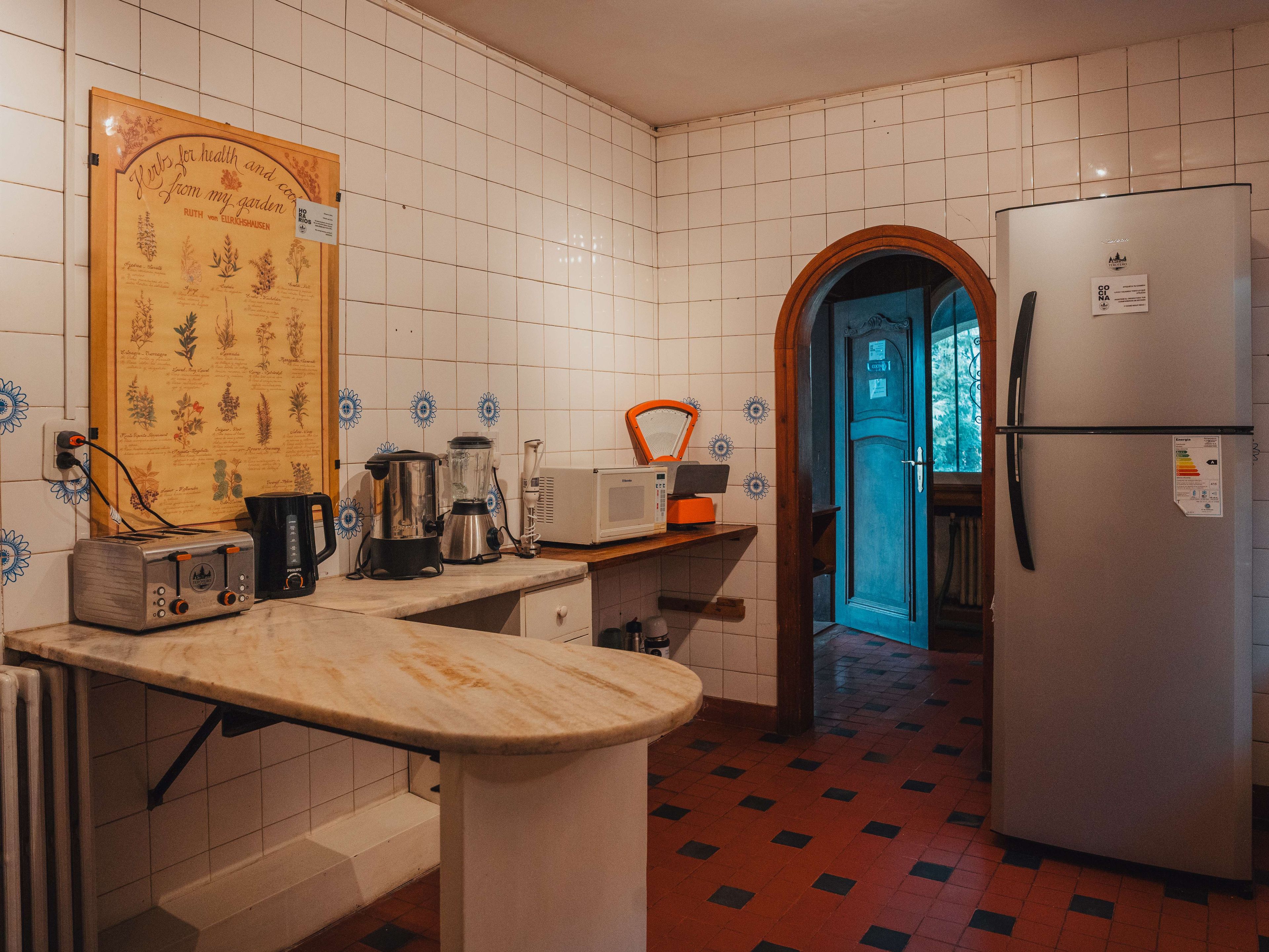A kitchen with a tiled backsplash, a refrigerator, a toaster, a blender, and a coffee maker.