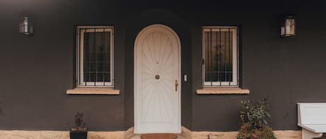 A building with a white door, two windows with bars, and a small porch area.