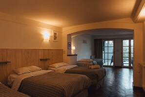 Een hotelkamer met vier bedden op een rij, een houten hoofdeinde, een klein tafeltje en een deur naar een balkon.