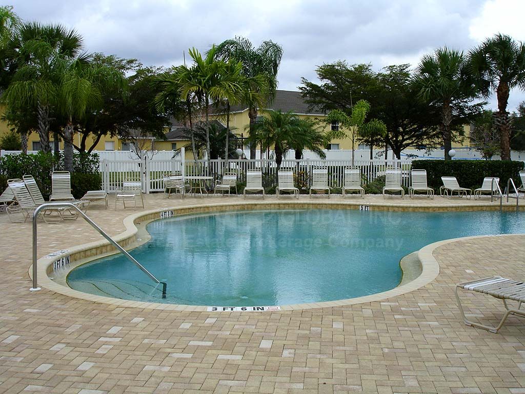 Une piscine entourée d’une clôture blanche, avec des chaises longues et des palmiers.