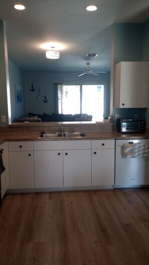 A kitchen with a sink, cabinets, a microwave, and a ceiling fan.