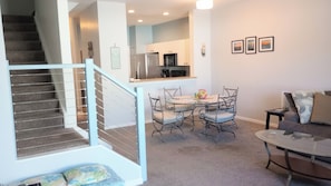A modern kitchen with stainless steel appliances, a dining area with a round table and metal chairs, and a staircase with a blue railing. - Fantastic 2-bedroom townhome in sunny Fort Myers with private back yard. (Fort Myers)
