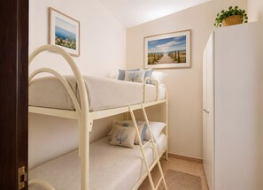 A bunk bed room with a door, two framed pictures on the wall, and a small plant on top of a cabinet.