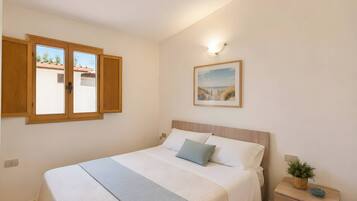 A bedroom with a bed, a nightstand, a wall-mounted picture, and a window with wooden shutters.