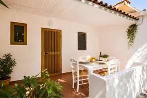 A patio with a white table set for dining, surrounded by potted plants and a wooden door.