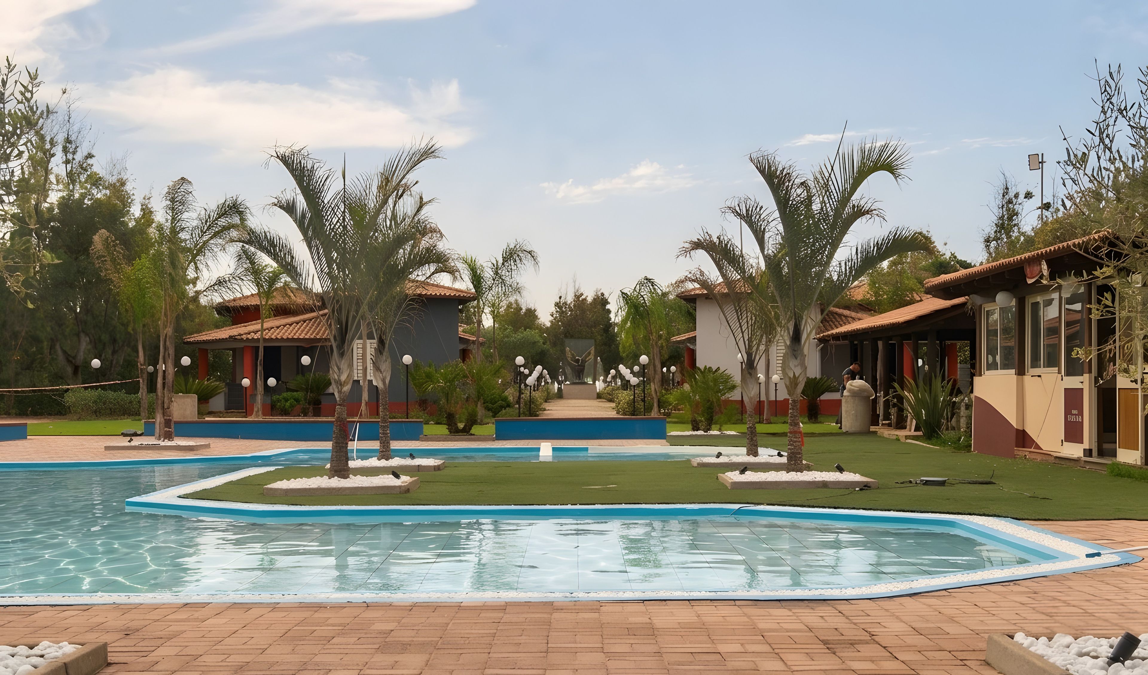 A swimming pool surrounded by palm trees and a building with a tiled roof.