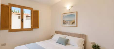 A bedroom with a bed, a nightstand, a wall-mounted picture, and a window with wooden shutters.