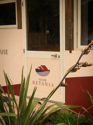 Ein Gebäudeeingang mit einem Schild, auf dem 'HOUSE BETANIA' steht, und einer Tür mit einem Griff.