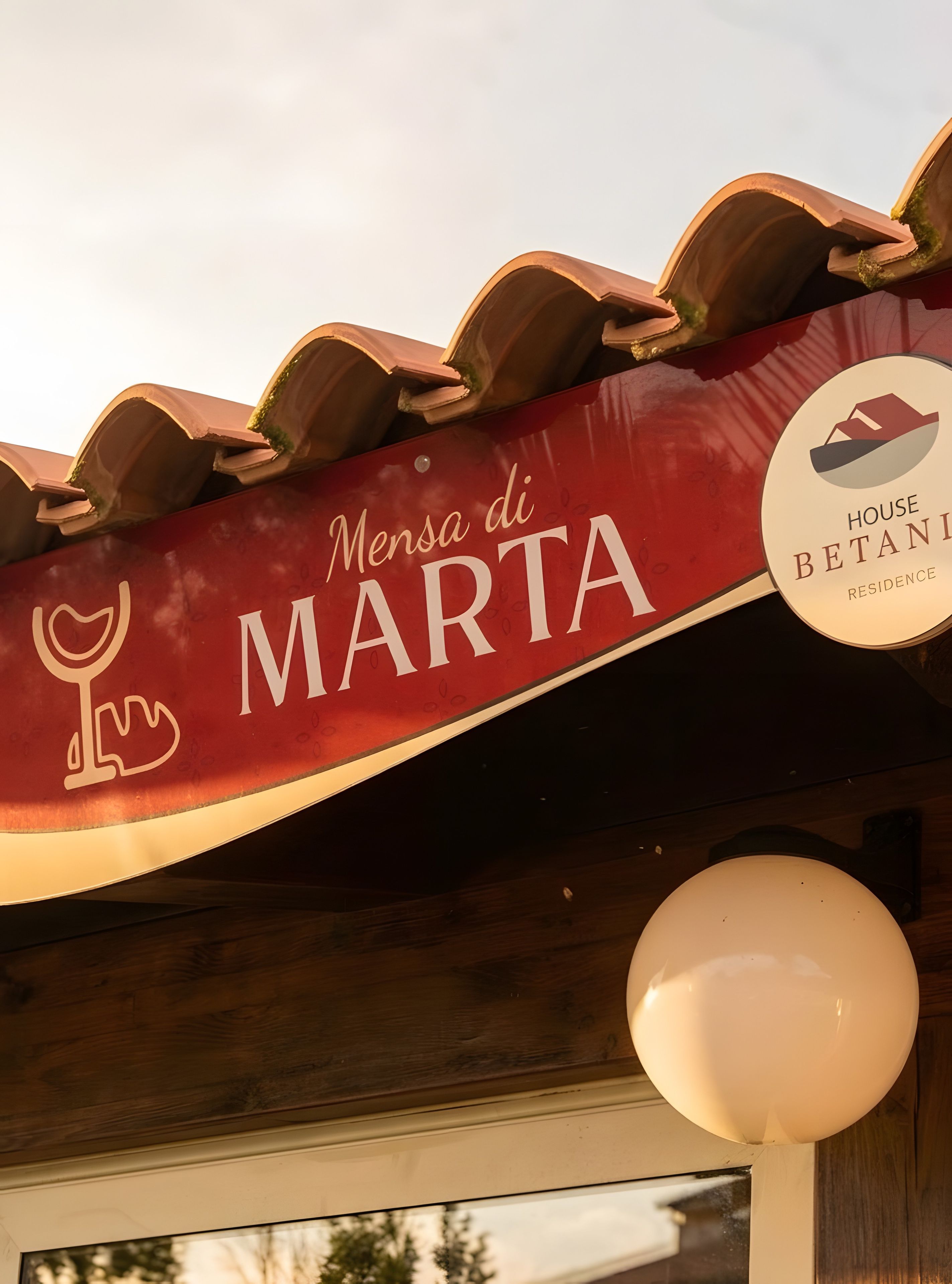 Un toldo rojo con el texto 'Mensa di MARTA' y el logotipo de 'HOUSE BETANI RESIDENCE'.