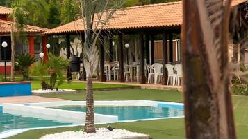 Ein Swimmingpool mit einer Palme, umgeben von einer überdachten Terrasse mit Stühlen und Tischen.