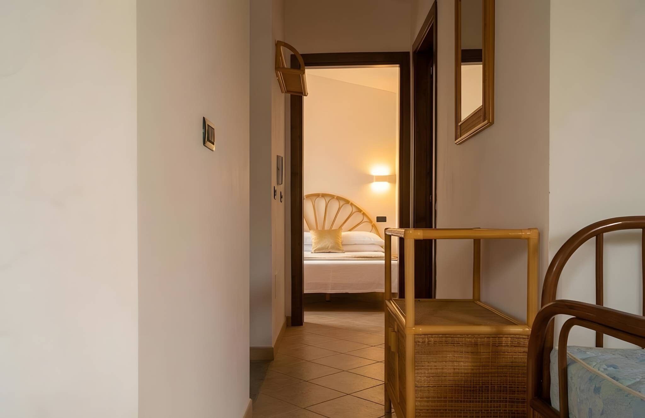 A hallway leading to a bedroom with a bed, a chair, and a nightstand.