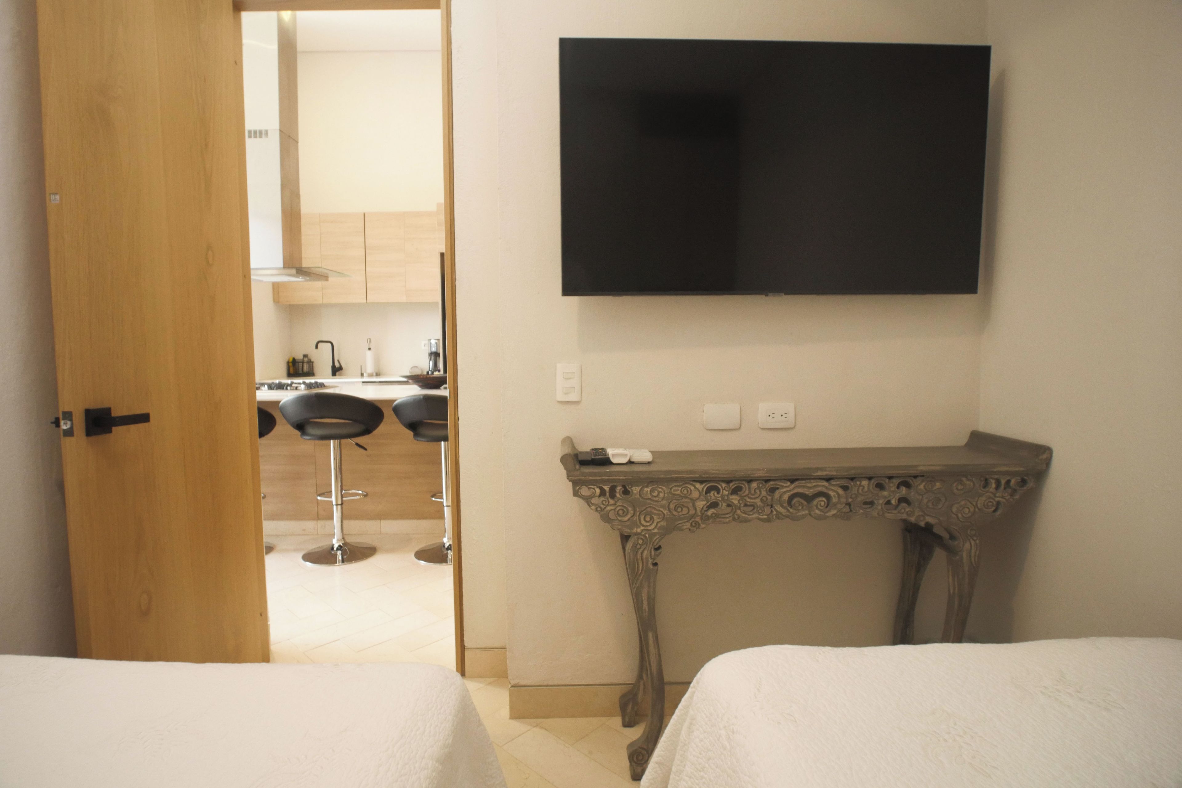 Ett hotellrum med en TV som är monterad på väggen, ett litet bord och två sängar.