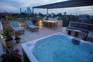 Terraza en la azotea con jacuzzi, sillas de descanso, mesa de comedor y plantas en macetas.