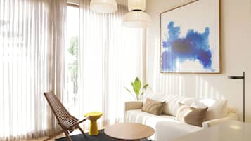 Uma sala de estar moderna com um sofá, uma poltrona, uma mesa redonda e um grande quadro abstrato.