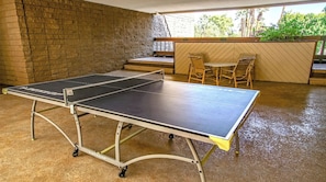 Une table de ping-pong installée dans un espace extérieur, avec un mur en briques et une terrasse en bois.