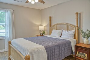 Een slaapkamer met een houten bed, een nachtkastje met een lamp, een radio en een raam met gordijnen.