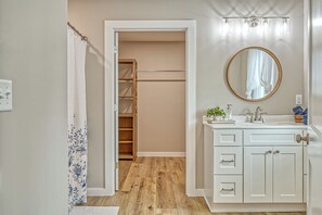 Een badkamer met een houten vloer, een wit aanrecht met een spiegel en een inloopkast met een houten deur.