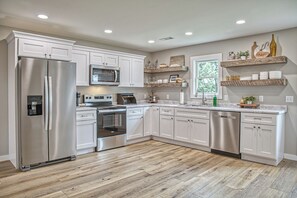 A modern kitchen with stainless steel appliances, white cabinetry, and a herringbone wood floor.