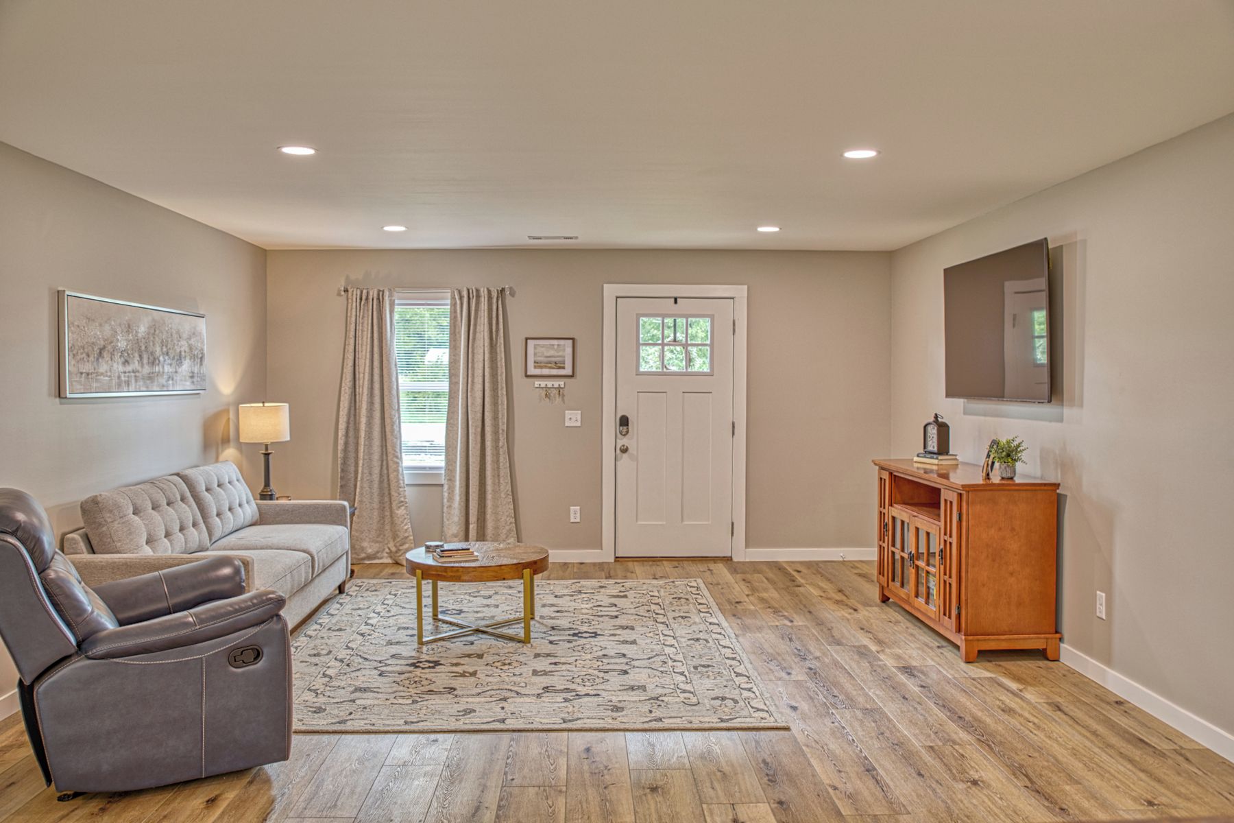 A living room with a sofa, a recliner, a coffee table, a rug, a door, a cabinet, and a television.