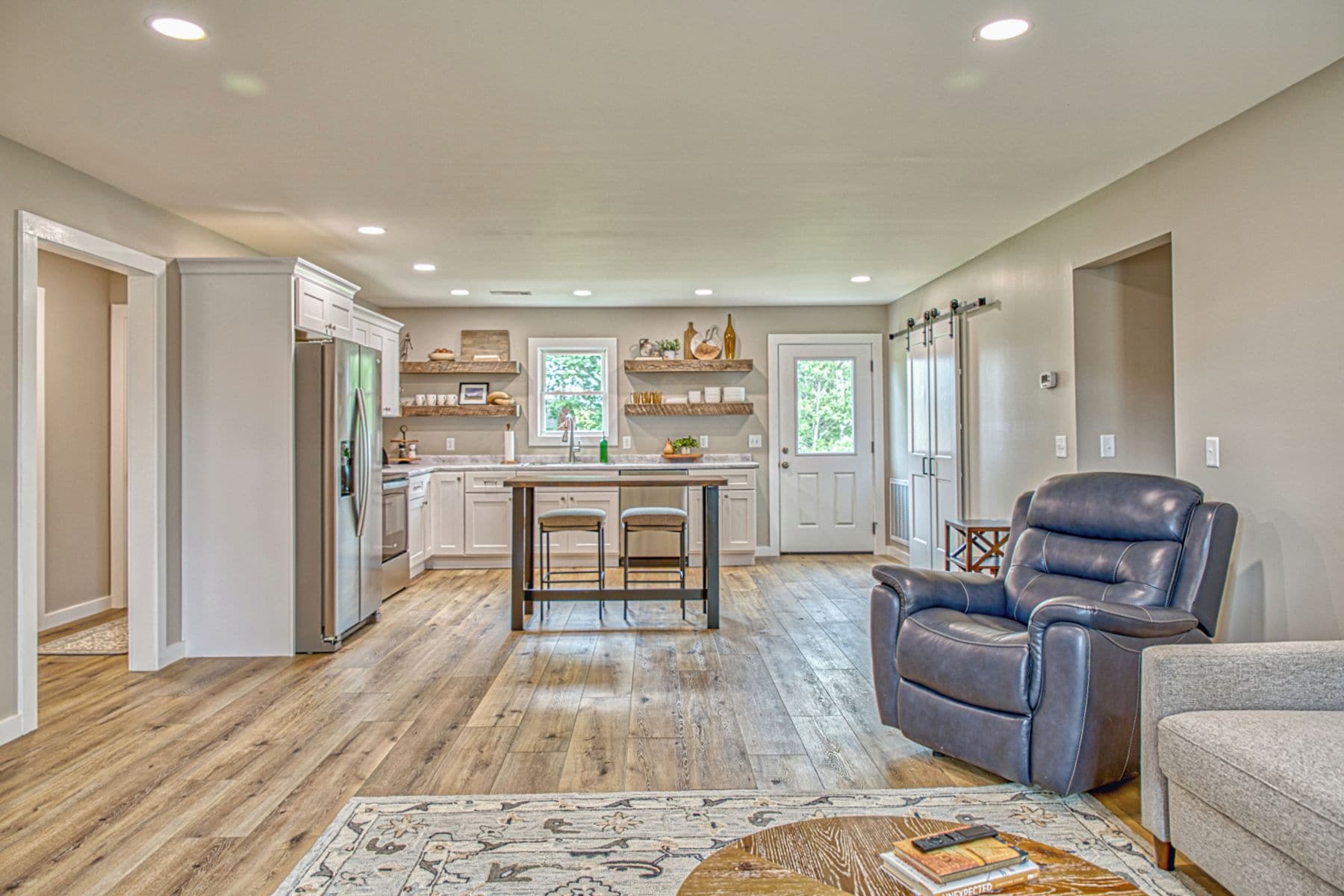 A spacious kitchen with a central island, wooden flooring, and a dining area with a leather chair.