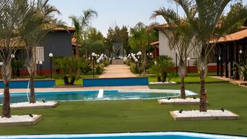 A pool area with a clear pathway leading to a building, surrounded by palm trees and a well-maintained lawn.