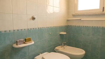 A bathroom with a toilet, bidet, and a shelf with toiletries.