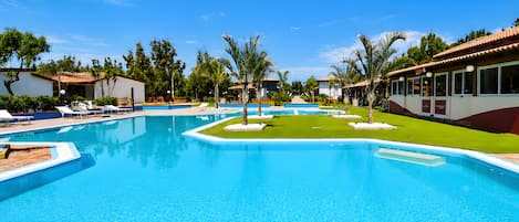 A swimming pool with lounge chairs and palm trees, surrounded by buildings with a tiled roof.