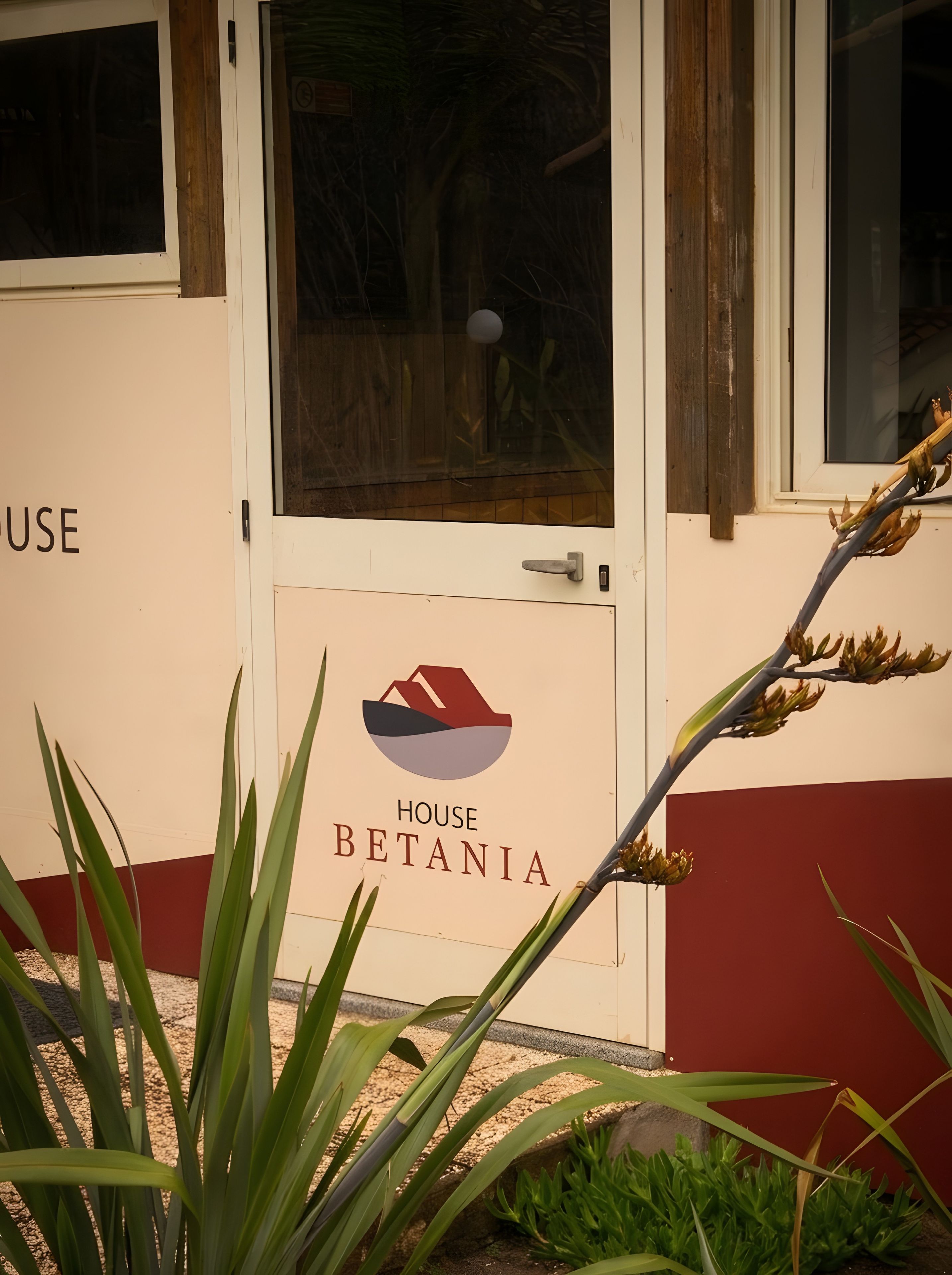 Ein Gebäudeeingang mit einem Schild, auf dem 'HOUSE BETANIA' steht, und einer Tür mit einem Griff.