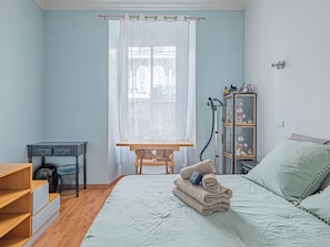 Quarto com cama, escrivaninha, cadeira, guarda-roupa e janela com cortinas.