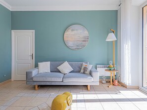 Sala de estar com sofá, pintura redonda, luminária e um urso de pelúcia no chão.