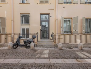 Een gebouw met een verharde oprit, een scooter ervoor en een metalen hekwerk.