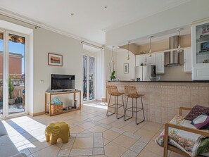 A modern kitchen with a dining area, a television, and a small table with chairs. - 3 chambres & terrasse - Aux portes de Monaco (Beausoleil)