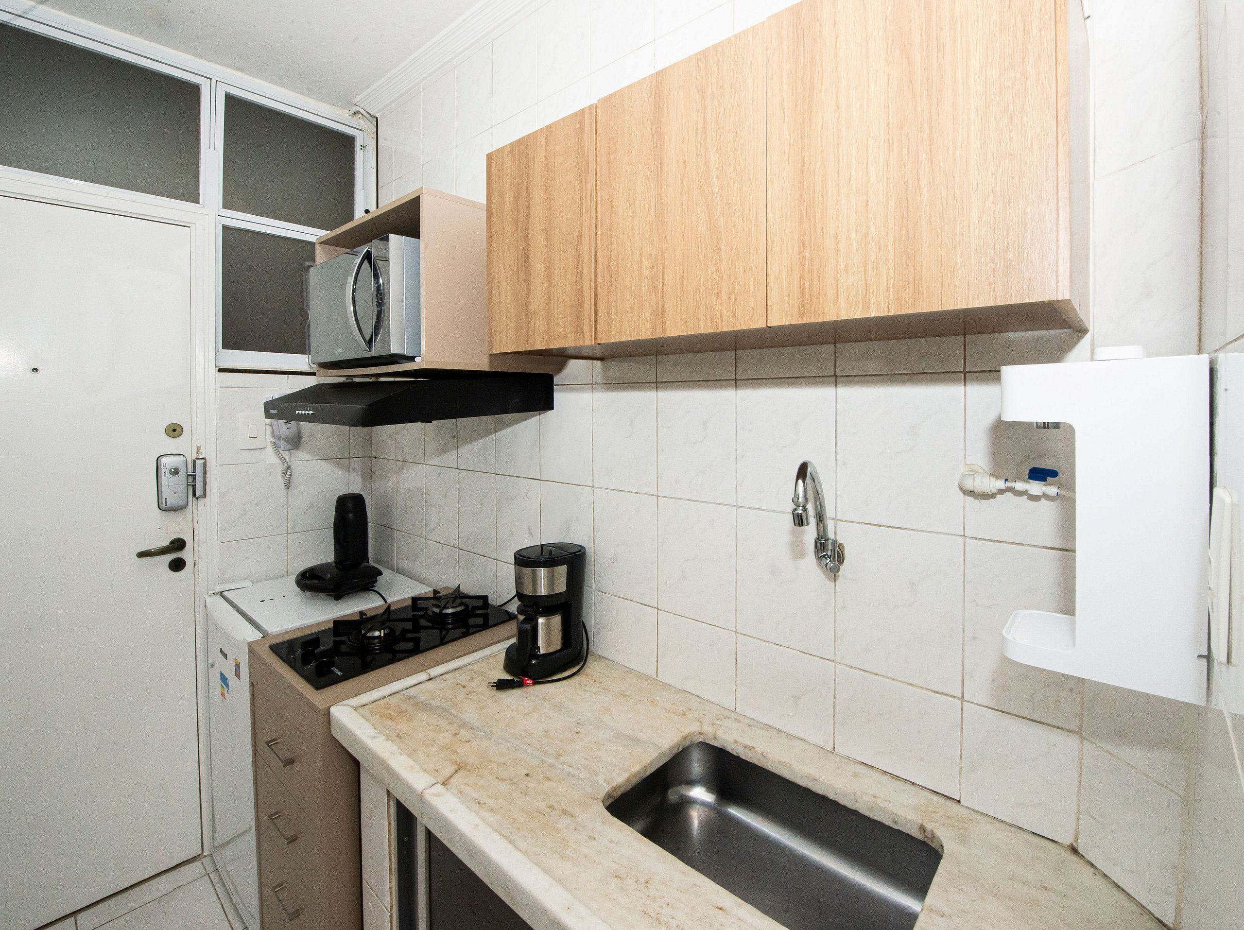 A compact kitchen with a built-in microwave, a coffee maker, a sink, and wooden cabinets.
