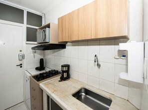 A compact kitchen with a built-in microwave, a coffee maker, a sink, and wooden cabinets.