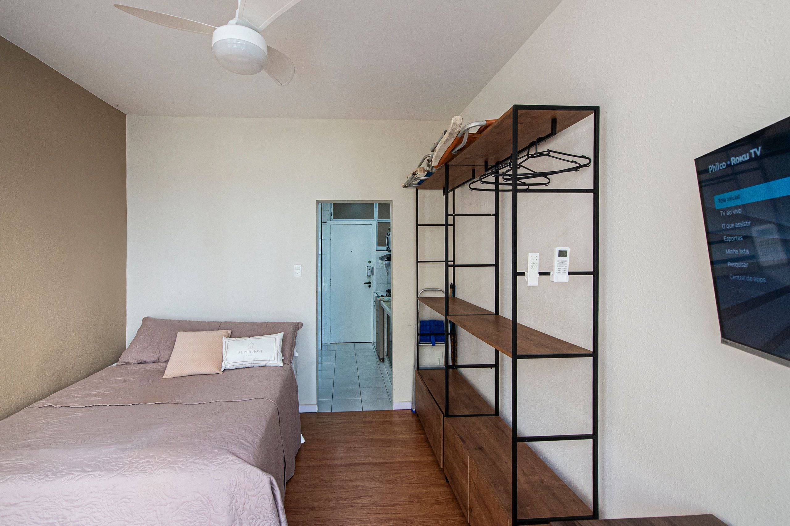 A bedroom with a bed, a wardrobe, a TV, and a ceiling fan.