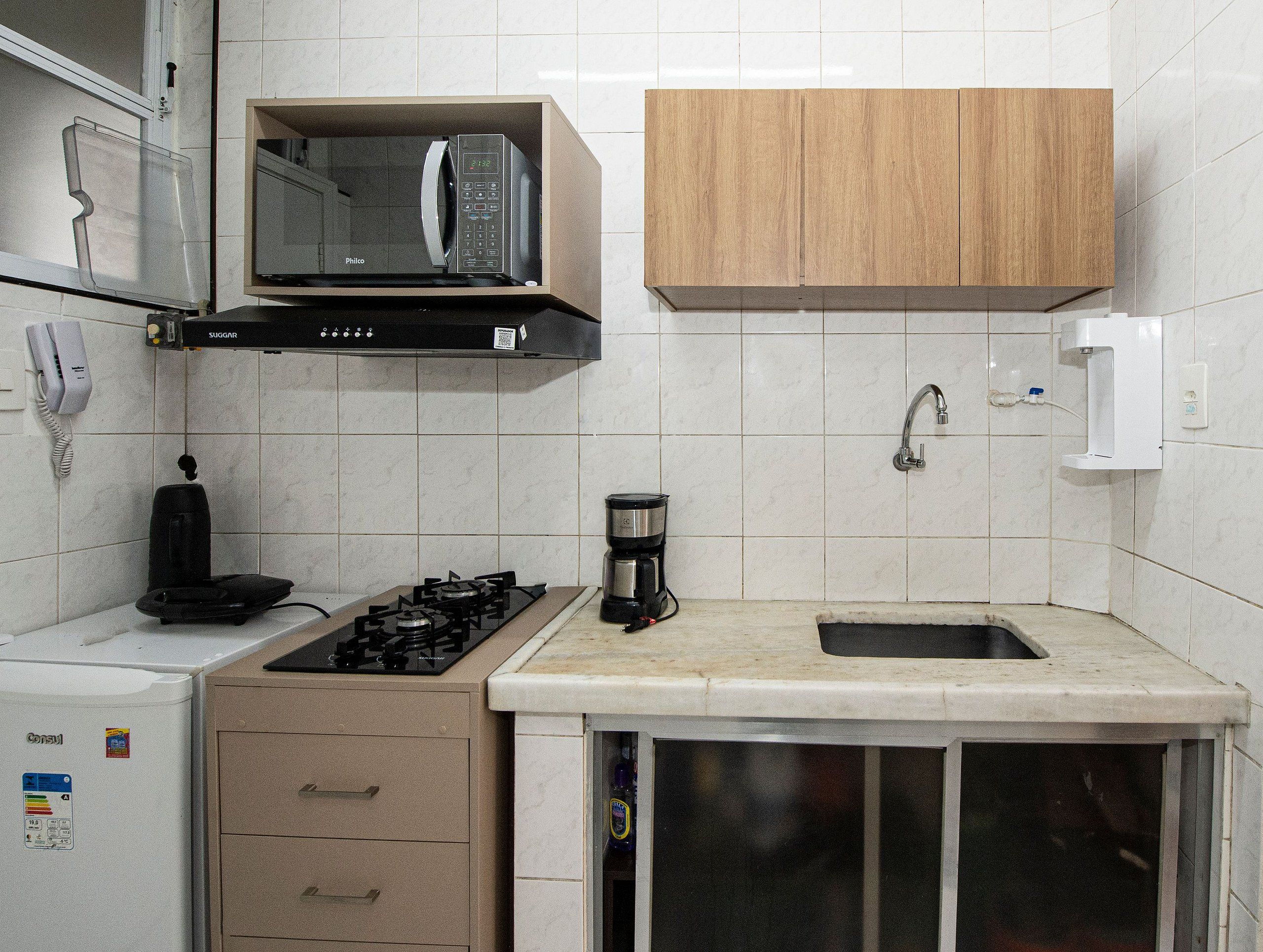 A compact kitchen with a microwave, gas stove, coffee maker, and a small sink.