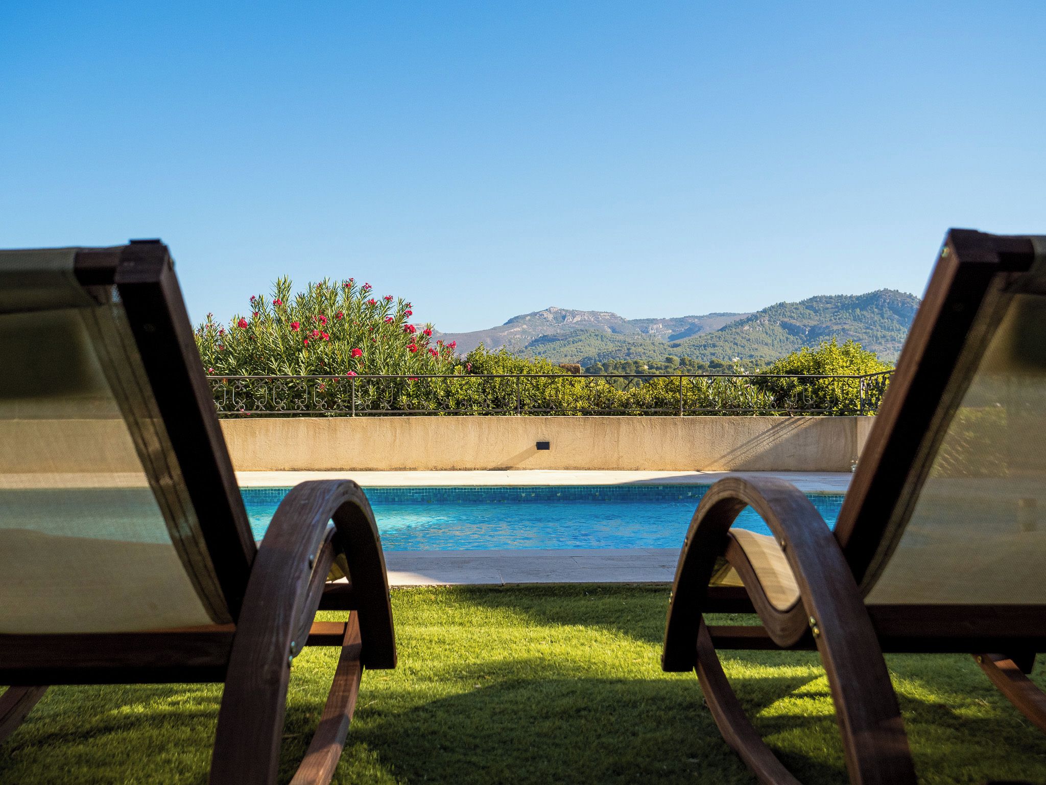 Two lounge chairs facing a swimming pool with a view of mountains and a garden with red flowers.