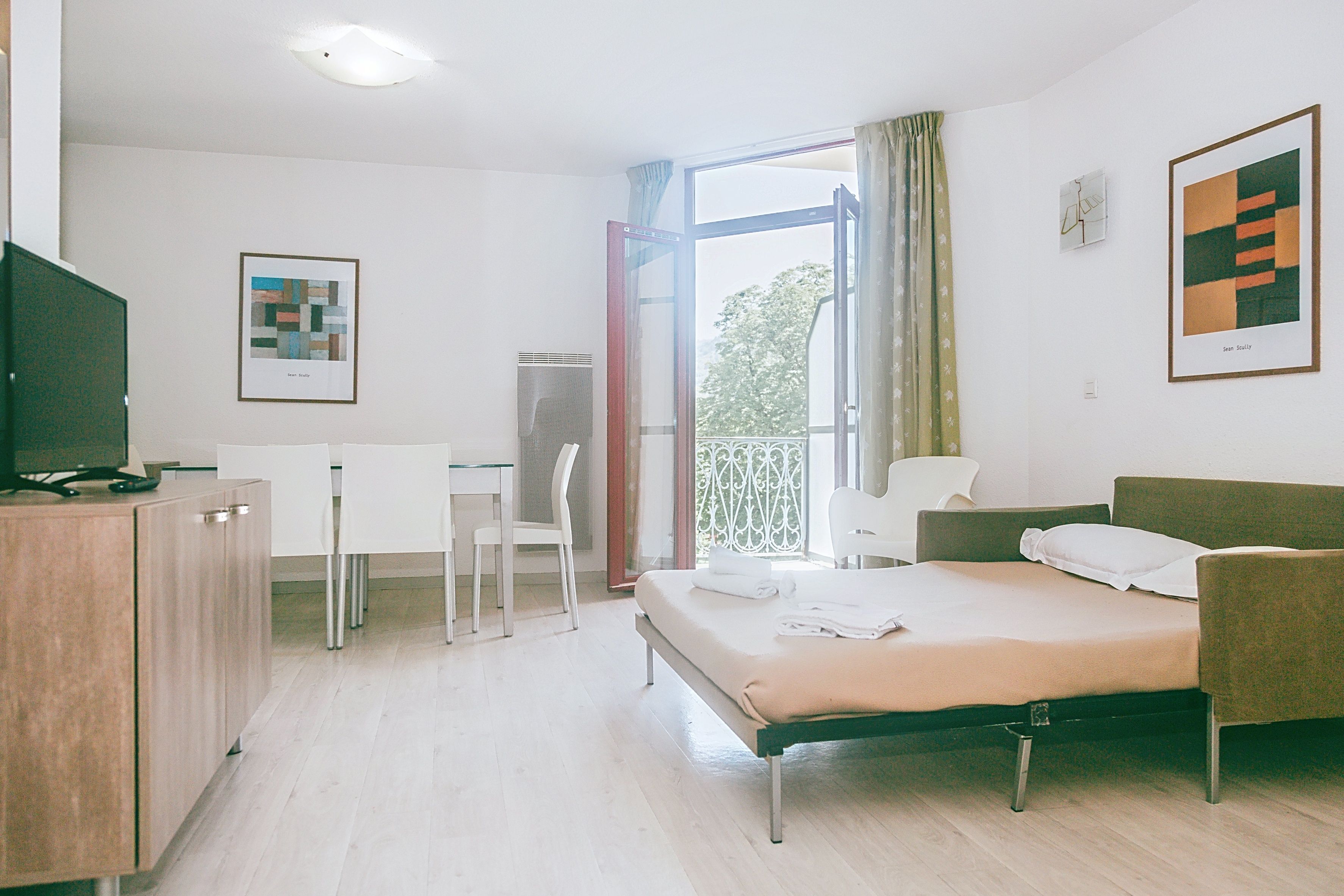 Une chambre d’hôtel équipée d’un lit, d’un bureau, d’une chaise, d’une télévision et décorée avec des œuvres d’art aux murs.