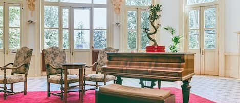 Huone, jossa on suuri flyygeli, penkki ja kaksi nojatuolia.
