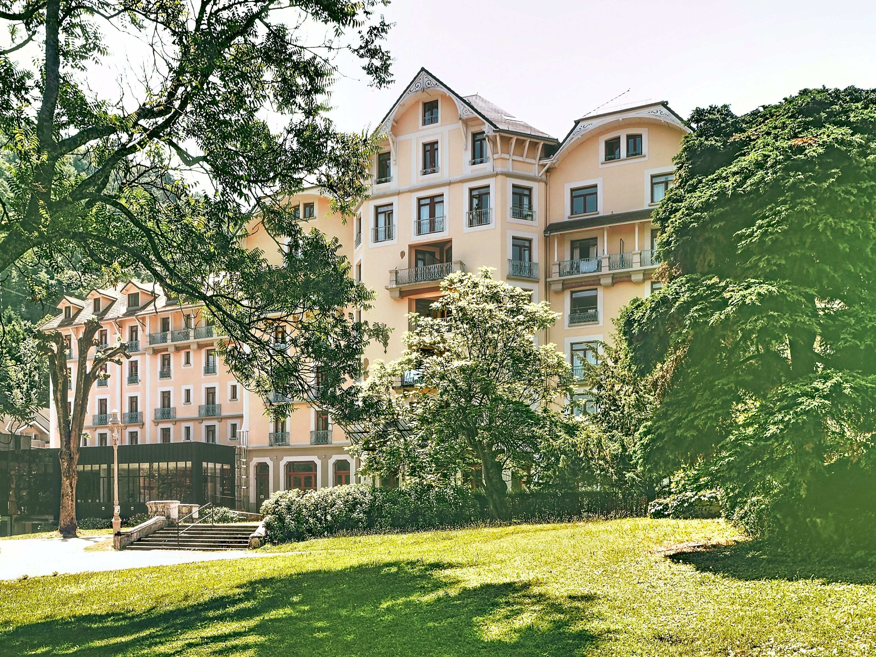 Un immeuble à plusieurs étages doté de balcons, entouré d’une végétation luxuriante et d’une pelouse bien entretenue.