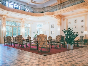 Une vaste pièce agrémentée de colonnes richement décorées, d’un tapis rouge et d’une grande plante en pot.