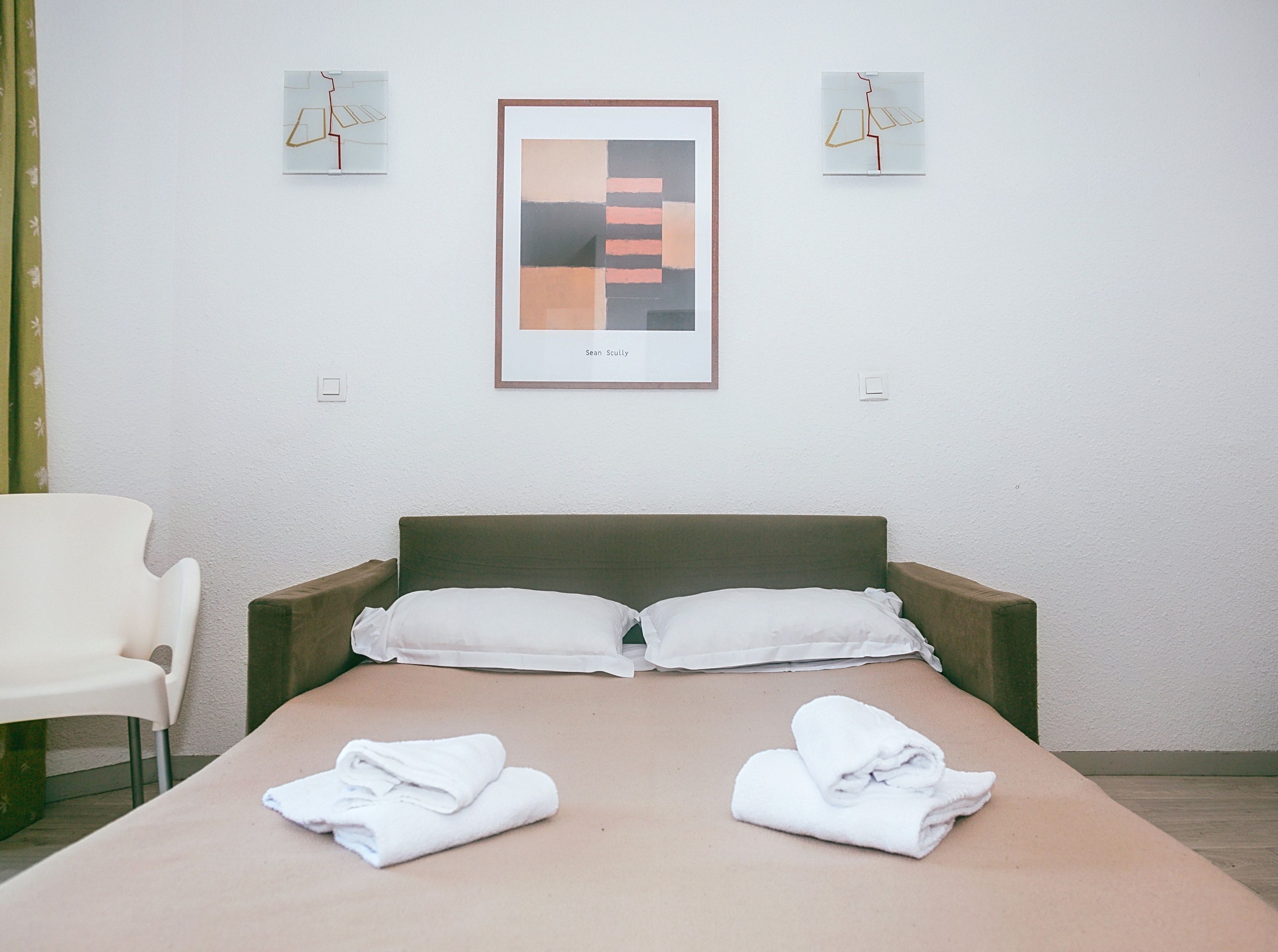 Ein Hotelzimmer mit einem Bett, zwei Kissen, einem Sessel und zwei Wandleuchten.