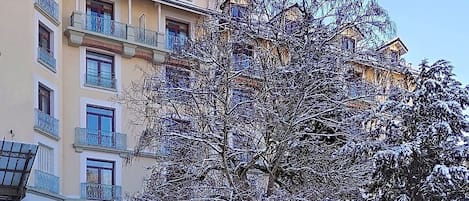 A multi-story building with balconies and a snow-covered tree in front.